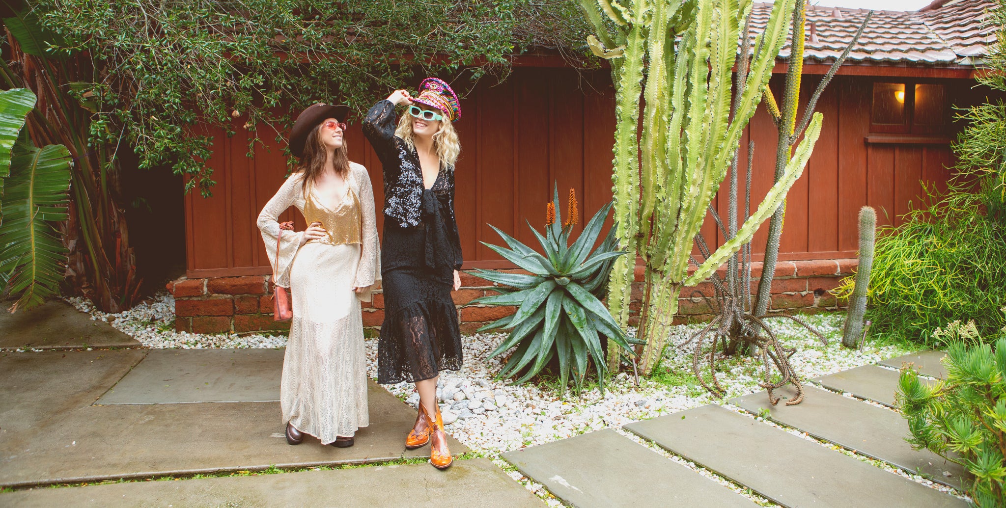 two girls dressed up in hats and dresses in a succulent filled garden ready for festival season. 