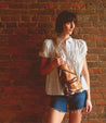 A versatile woman in shorts and a white shirt holding a practical Bed Stu Andie leather sling bag.