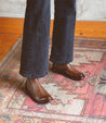 An individual, stylishly dressed in jeans and Bed Stu Barfly Chelsea boots, stands confidently on a rug.