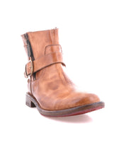 The Bed Stu Becca is a brown leather short engineer boot with an ankle buckle, decorative strap, low heel, and side zipper, shown on a white background.