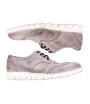 The Cayuga II by Bed Stu is a pair of oxford-style shoes in gray with white soles and brogue detailing, offering a casual male look when viewed from the side.