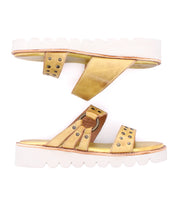 Bed Stu Chow gold and tan slip-on sandals with cushioned footbed and white scalloped chunky rubber soles, shown with one sandal facing up and the other facing down.