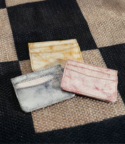 Three Chuck leather card holders by Bed Stu in yellow, pink, and gray rest elegantly on a woven checkered fabric background—ideal for organizing your credit cards or business cards with style.