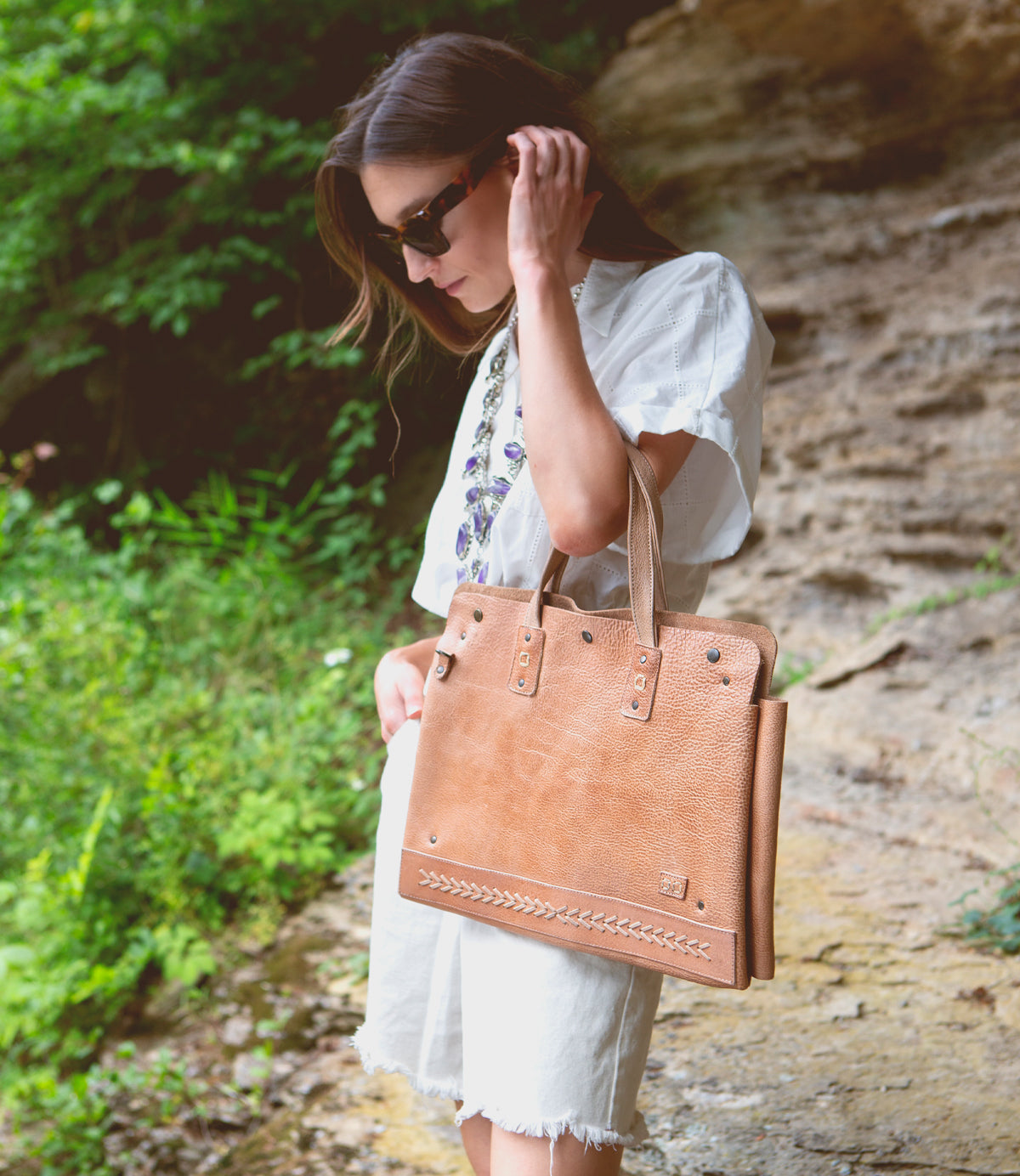 A Bed Stu commuter woman wearing white shorts and a tan leather tote, a multifunctional accessory for laptops.