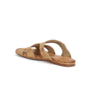 A single tan-colored slip-on leather sandal with crisscross straps, crafted from vegetable-tanned leather upper and viewed from the back and left side, is placed against a plain white background. The product is the Configure by Bed Stu.