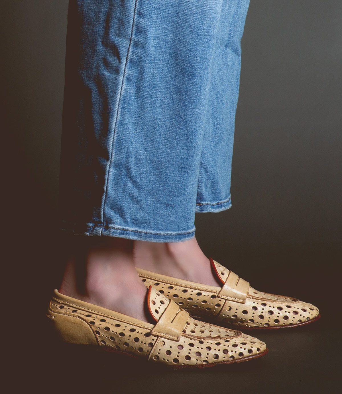 Person wearing blue jeans and tan loafers handcrafted in Italy with a playful cutout pattern called Cornflower by Bed Stu.