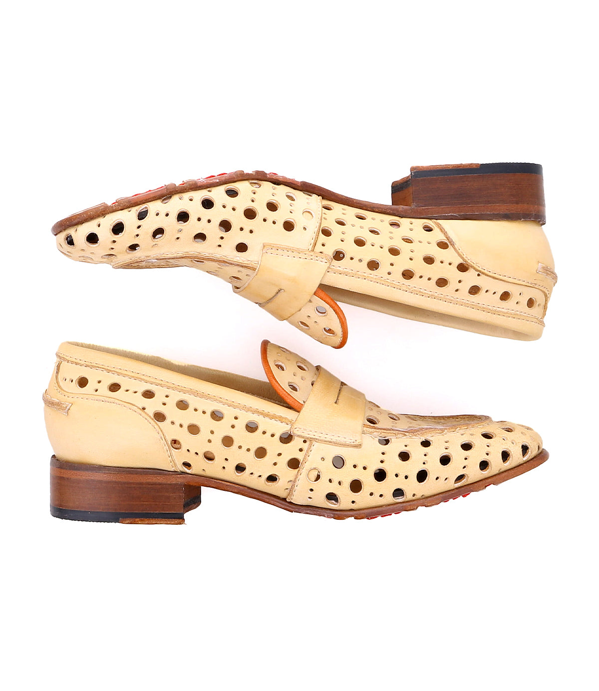 A pair of beige Cornflower loafers by Bed Stu with a playful circular cutout pattern, wooden heels, and leather straps. Handcrafted penny loafers are shown from the side, with one shoe upside down above the other.