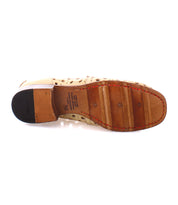 The sole of a handcrafted beige penny loafer features a playful circular cutout pattern. It showcases a wooden base with red stitching and a black heel. Size label "Cornflower" by Bed Stu and branding are clearly visible.