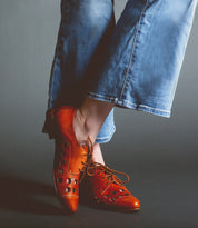 A person wearing blue denim jeans and brown leather handcrafted Bed Stu Decoy stands against a dark background.