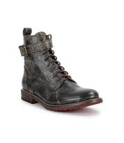 The Bed Stu Endure is a black lace-up ankle boot with a side buckle strap, rugged texture, leather lining, and a bold red rubber outsole, displayed on a white background.