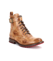 The Bed Stu Endure is a tan leather lace-up ankle boot with a buckle strap, low heel, and red rubber outsole for traction, shown on a white background.