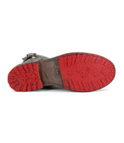 The Bed Stu Endure is a lace-up ankle boot with a brown leather upper and a rugged red rubber outsole featuring various patterns, shown sole up.