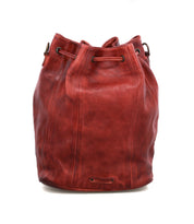 The Bed Stu Eve is a red leather bucket bag with a drawstring cinch and grommets, featuring a slightly textured finish and standing upright on a white background.