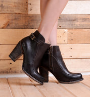 A woman wearing the Bed Stu Isla black leather ankle boots on a wooden floor.
