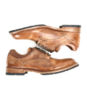 A pair of Bed Stu Fierce men’s brown leather derby shoes with black soles, stacked in opposite directions on a white background, blends classic and contemporary style.