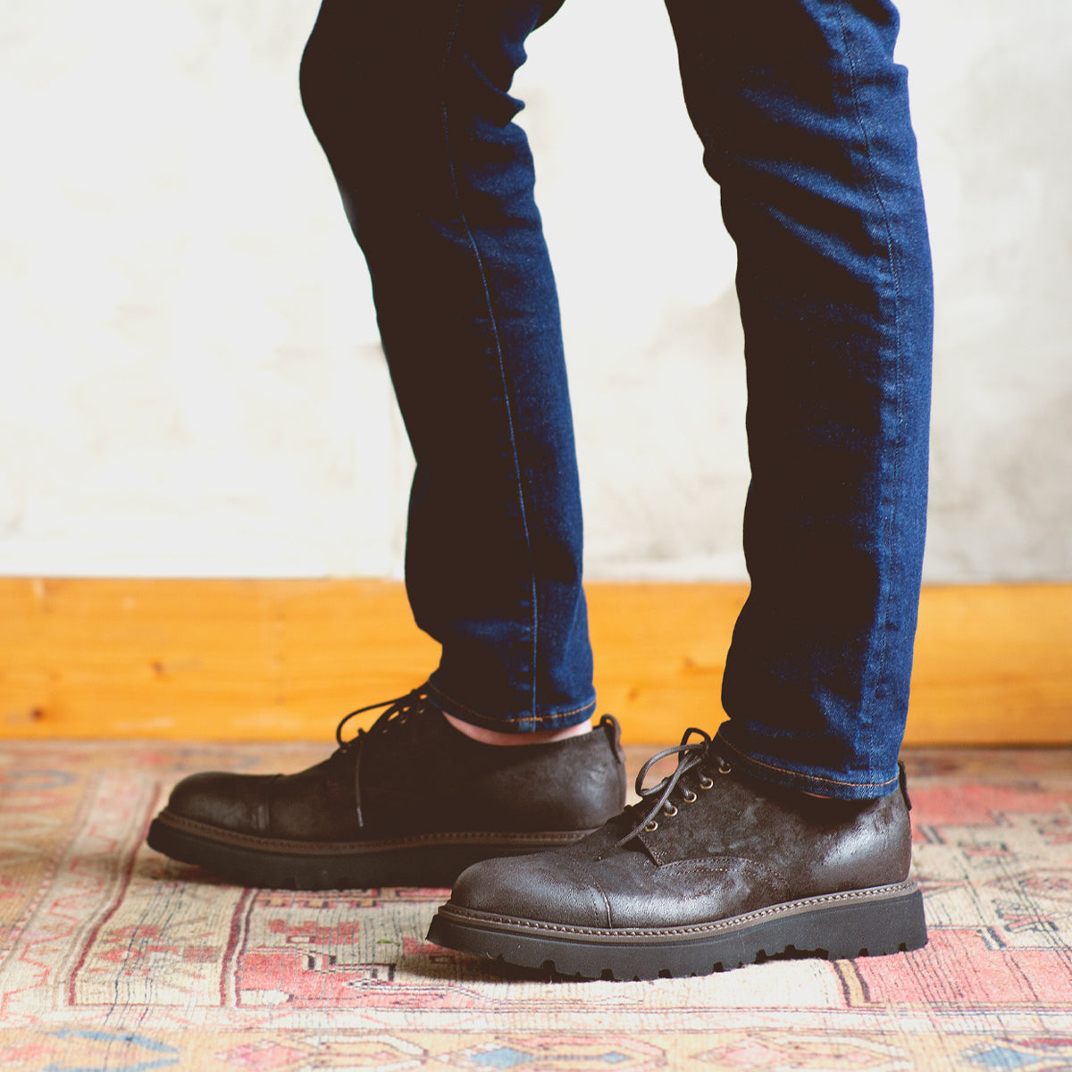 A man wearing jeans and a pair of Bed Stu Grant, standing on a rug.