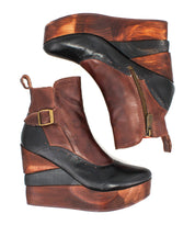 The Bed Stu Harmonious is a pair of brown and black leather Platform Wedge Ankle Boots featuring a sculptural wood wedge, side zipper, decorative buckle, and chic brogue-style perforations.