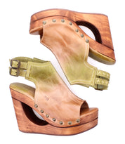 The Bed Stu Imelda sandals are tan leather wedges with wooden platforms, metal studs, double ankle buckles, and an open-toe design, shown from the side.