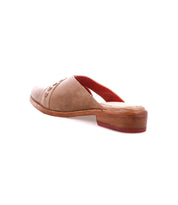 The Bed Stu Jockey is a tan leather slip-on with a sleek design, flat wooden sole, and red interior, shown in a photo highlighting the side and back view.