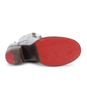 The Judgement boot by Bed Stu highlights a captivating gray exterior paired with a vibrant red sole, with the bottom view accentuating its detailed tread pattern and sturdy block heel. Its design effortlessly merges style and practicality, making it an essential addition to any wardrobe.