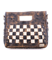 The Keiki bag by Bed Stu is a brown leather accessory featuring a built-in handle and a striking black and white checkerboard pattern on the front. It boasts a weathered, rustic look complemented by metallic rivet details. The adjustable strap allows for versatile crossbody wear, and the zip-top closure ensures added security.