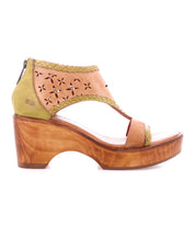 The Bed Stu Locket is a tan and olive green open-toe sandal with a vintage vibe, featuring a wooden platform heel, laser-cut floral details on the upper, and braided edge accents.