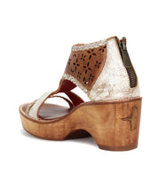 The Bed Stu Locket is a vintage-inspired sandal featuring metallic and brown leather, laser-cut floral details, artisanal craftsmanship, a wooden heel, and a convenient back zipper closure.