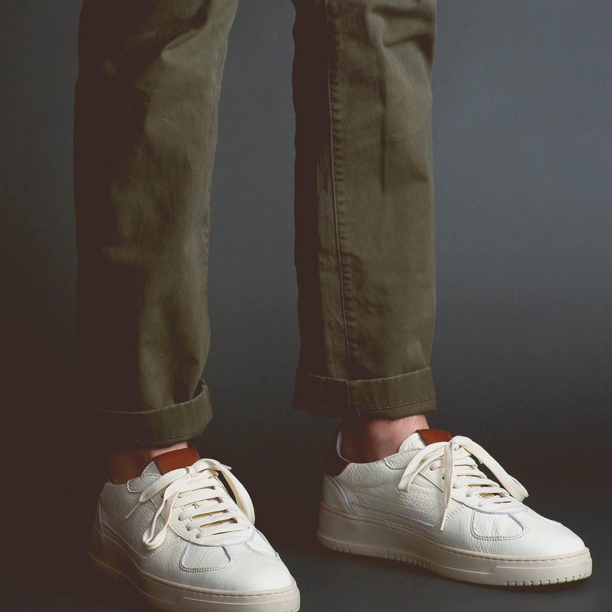 A person wearing olive green pants and North sneakers by Bed Stu, known for their high-quality leather, stands against a dark background.