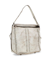 The "Packet LTC" by Bed Stu is a beige leather tote handbag featuring a single shoulder strap, decorative metal studs along the seams, and a top zipper closure, making it perfect for travel.