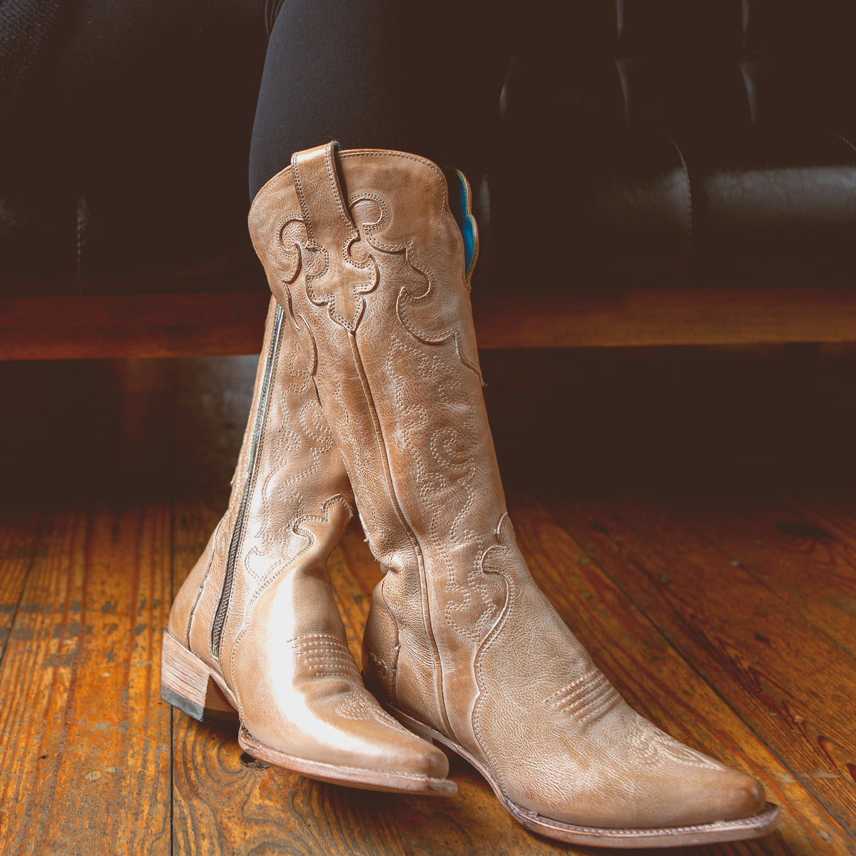 A Bed Stu Queen wearing a pair of tall tan boots adorned with fleur-de-lis designs.
