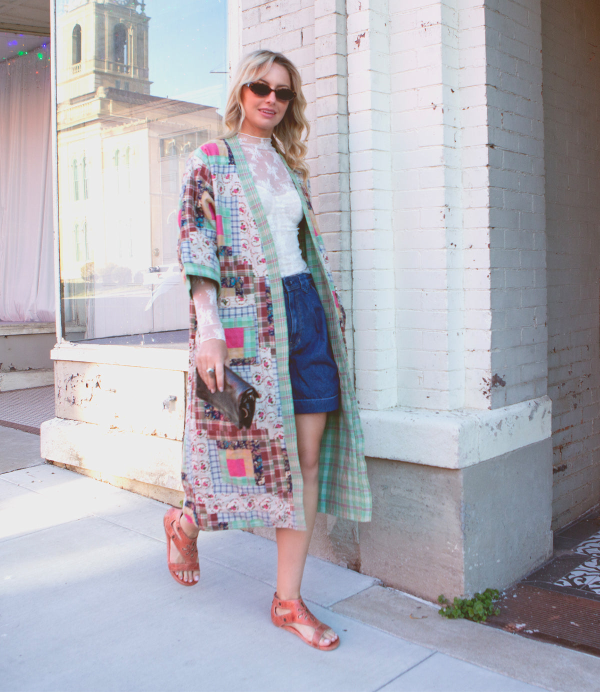 A woman in a colorful patchwork coat and sunglasses, posing on a city sidewalk, wearing Bed Stu Soto Cutout leather sandals.