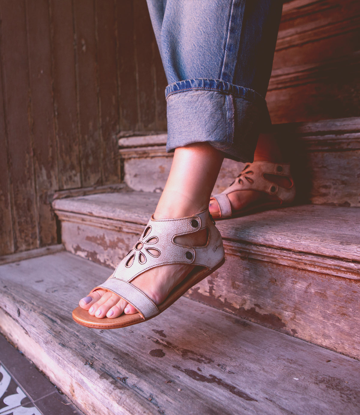 A person wearing Bed Stu Soto Cutout sandals resting their feet on wooden steps.