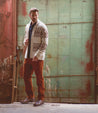 A man in a patterned cardigan and rust-colored pants wearing Bed Stu leather lace-up ankle boots stands confidently in front of a weathered teal door.