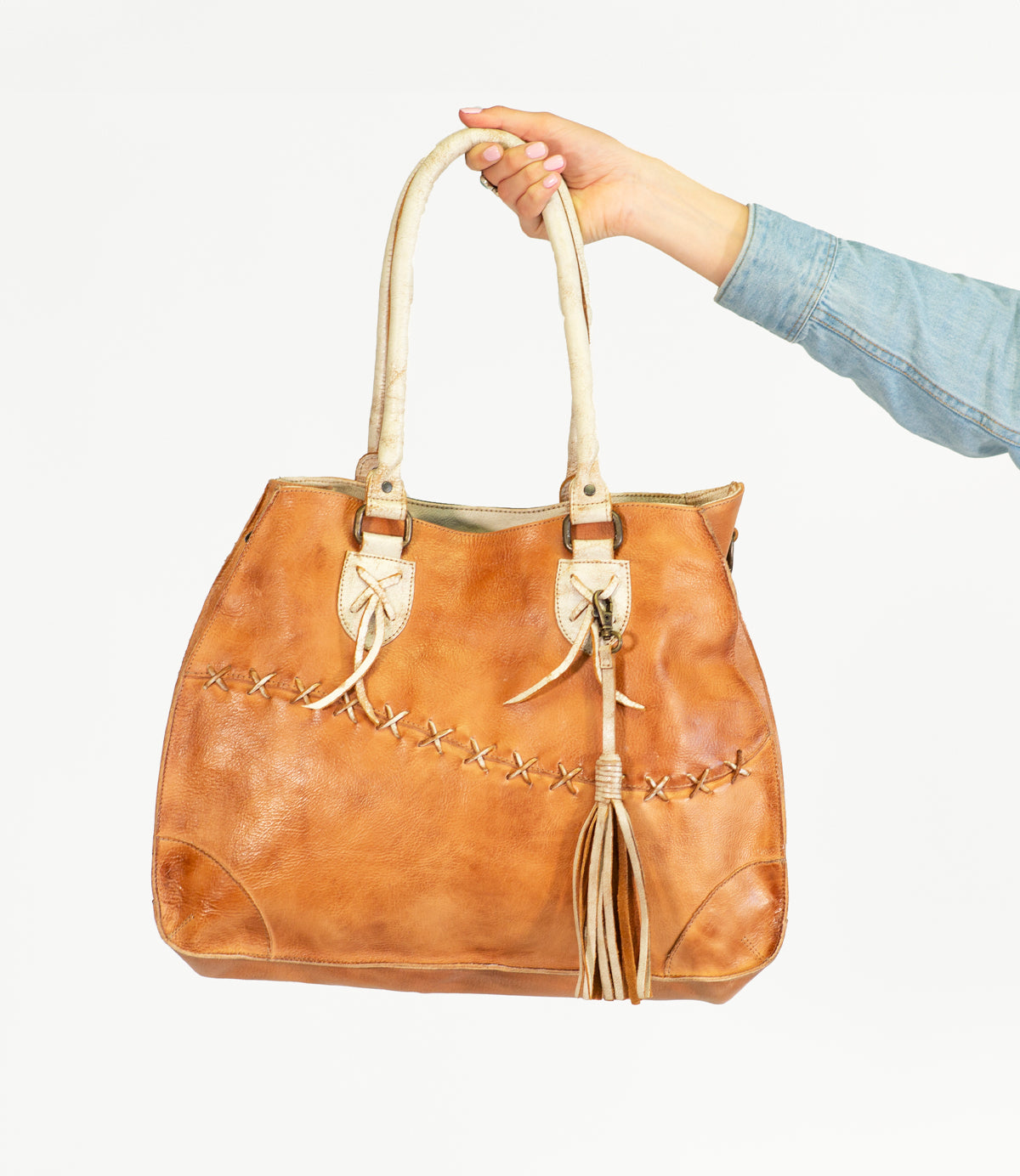 An accessory with tassels, the Bed Stu brown leather bag is being held by a hand, showcasing personal expression.