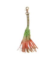 The Bed Stu Tassel Clip features a multicolored ombre tassel with a metal clasp and high-quality leather strap, showcasing personal expression as the colors shift from green to orange and beige.