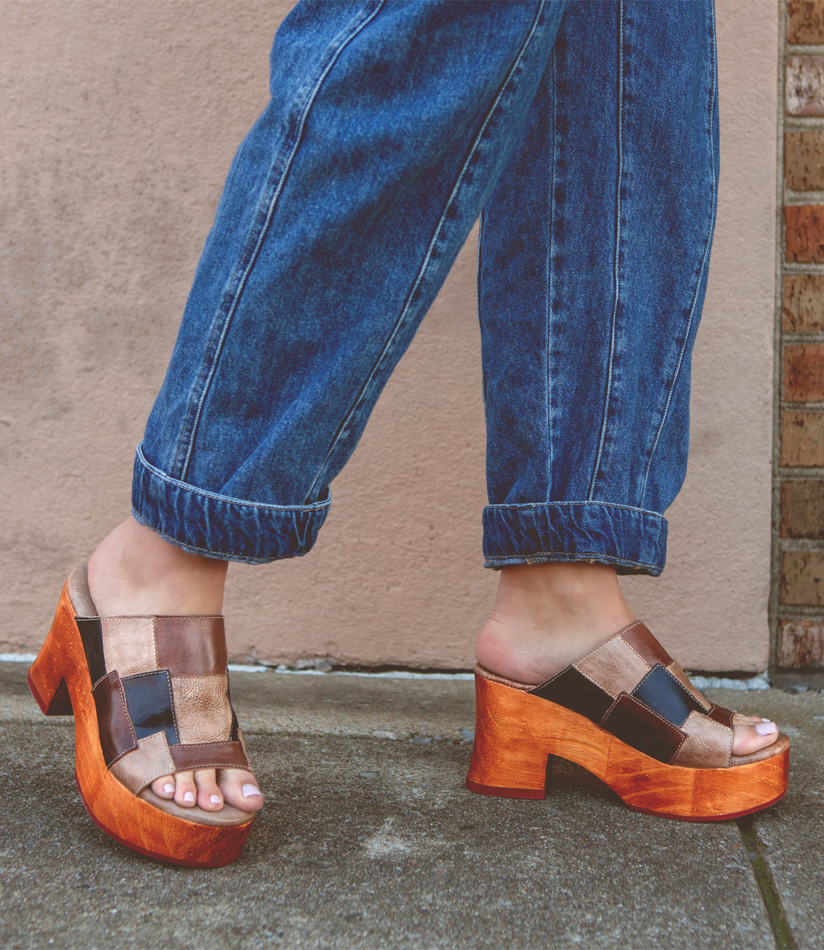 A person wearing blue jeans and Bed Stu's environmentally-conscious Vanquish mules standing against a wall.