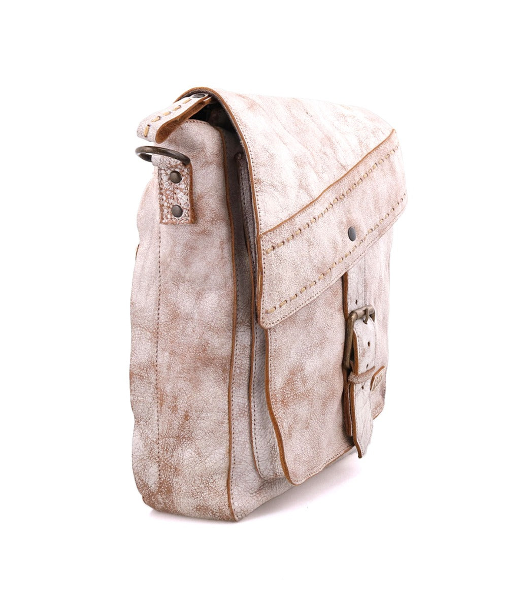 A worn, beige leather Ainhoa LTC crossbody handbag by Bed Stu with an adjustable strap and buckle closures, standing against a white background.