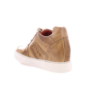 The Andromeda by Bed Stu is a tan leather high-top sneaker with white soles, viewed from the back and side. It features intricate stitching details, a lace-up design, and a hidden heel for that street-smart look.
