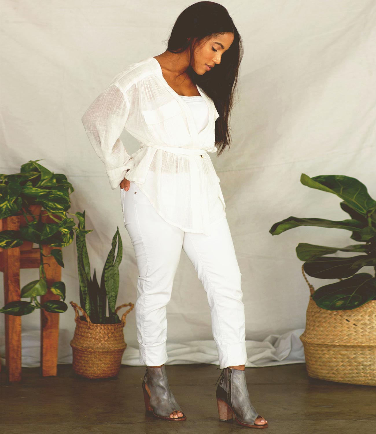 A woman in white pants and heels standing in front of a potted plant wearing Angelique boots by Bed Stu.