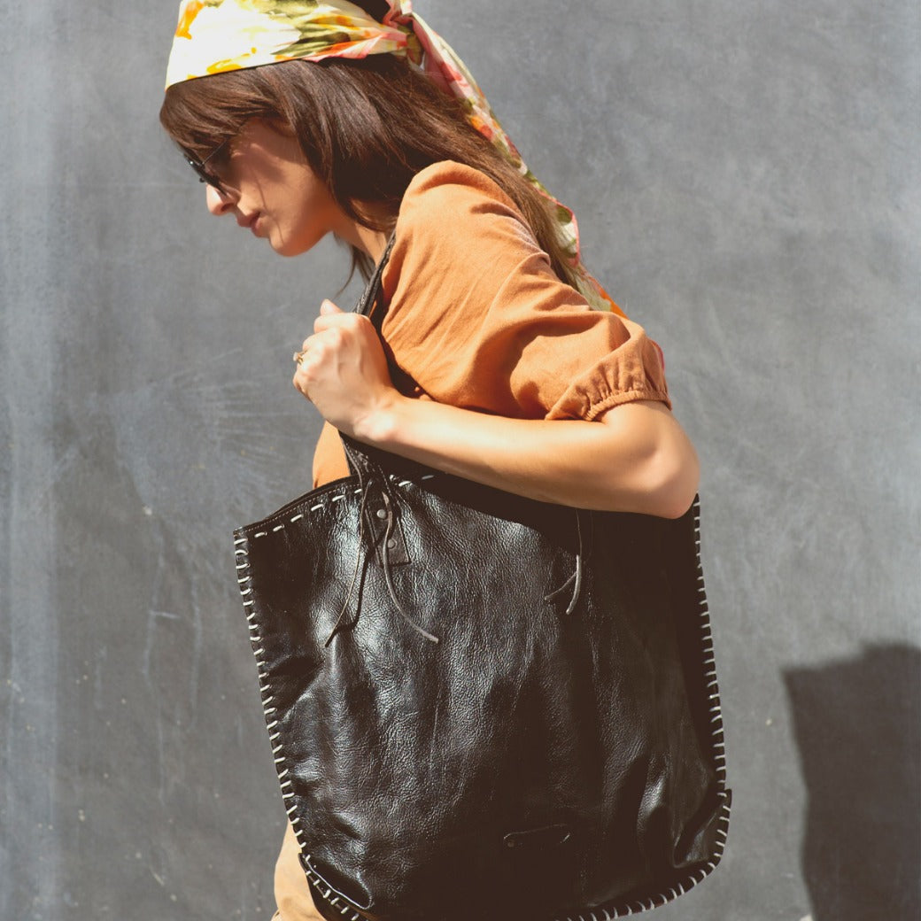 A woman carrying a black leather Bed Stu Barra tote bag.