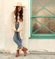 A woman in Bed Stu jeans and a Bed Stu hat leaning against a wall.