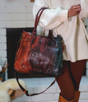 A person in a cream sweater and brown leggings holds the Bed Stu Bruna, a large two-toned leather bag with double handles and shoulder strap, highlighting its artisanal craftsmanship.