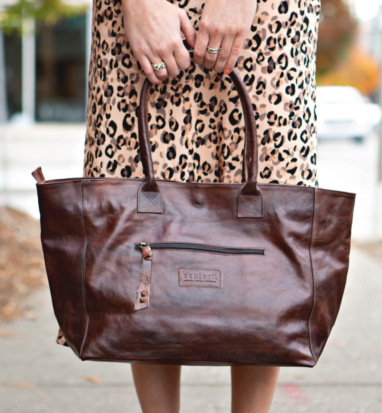 A woman in a leopard print Cersei dress holding a Bed Stu brown leather tote.