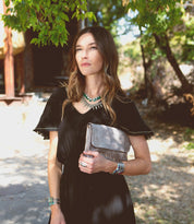 A woman wearing a black dress holding a Bed Stu Cleo clutch.