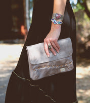 A woman wearing a black dress holding a Bed Stu Cleo clutch.