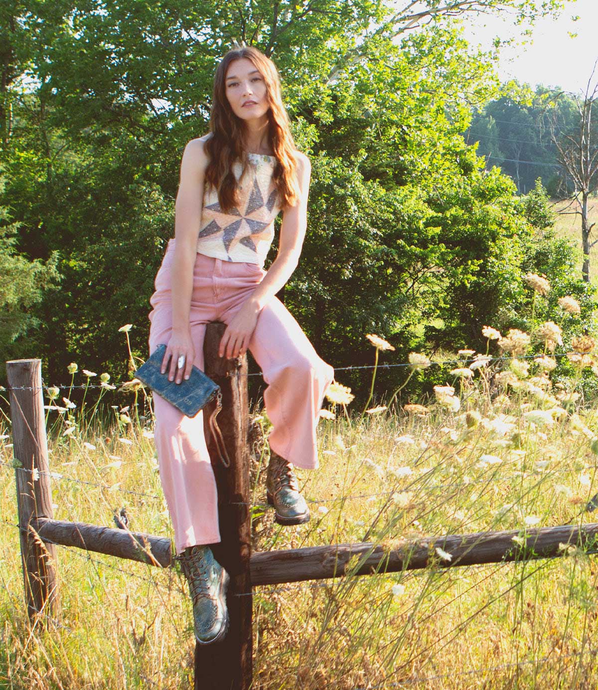 A woman is sitting on a fence in a field wearing Elisha II boots by Bed Stu.