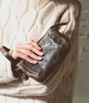 A woman wearing a sweater holding a Bed Stu Encase leather purse.