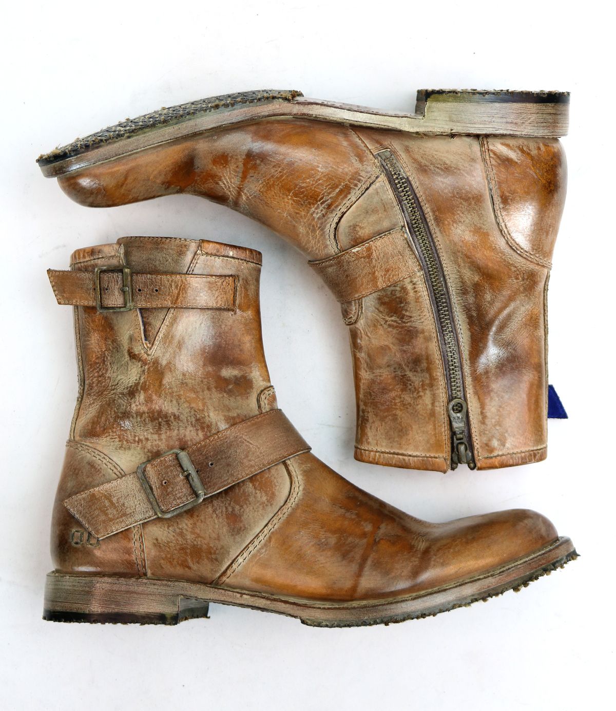 A pair of well-loved leather ankle boots, styled with moto-inspired buckles and zippers from Bed Stu's Fellow collection, displayed on their sides against a white backdrop.