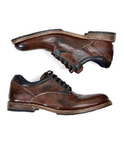 The Bed Stu Fierce shoes are a pair of worn, brown leather men's derby shoes with black laces and scuffed soles, showcasing a classic design with a touch of modern flair, set against a white background.