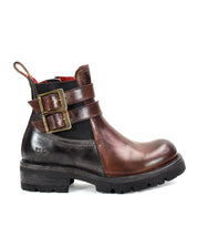 The Ginger II by Bed Stu is a brown leather Chelsea ankle boot, featuring two buckled straps on the side, a pull tab at the heel, and a thick black sole. It also includes stylish touches such as an inner zipper for easy wear.